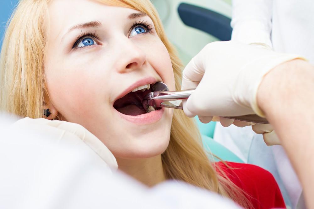 Dentist extracting a tooth from a female patient during dental procedure.
