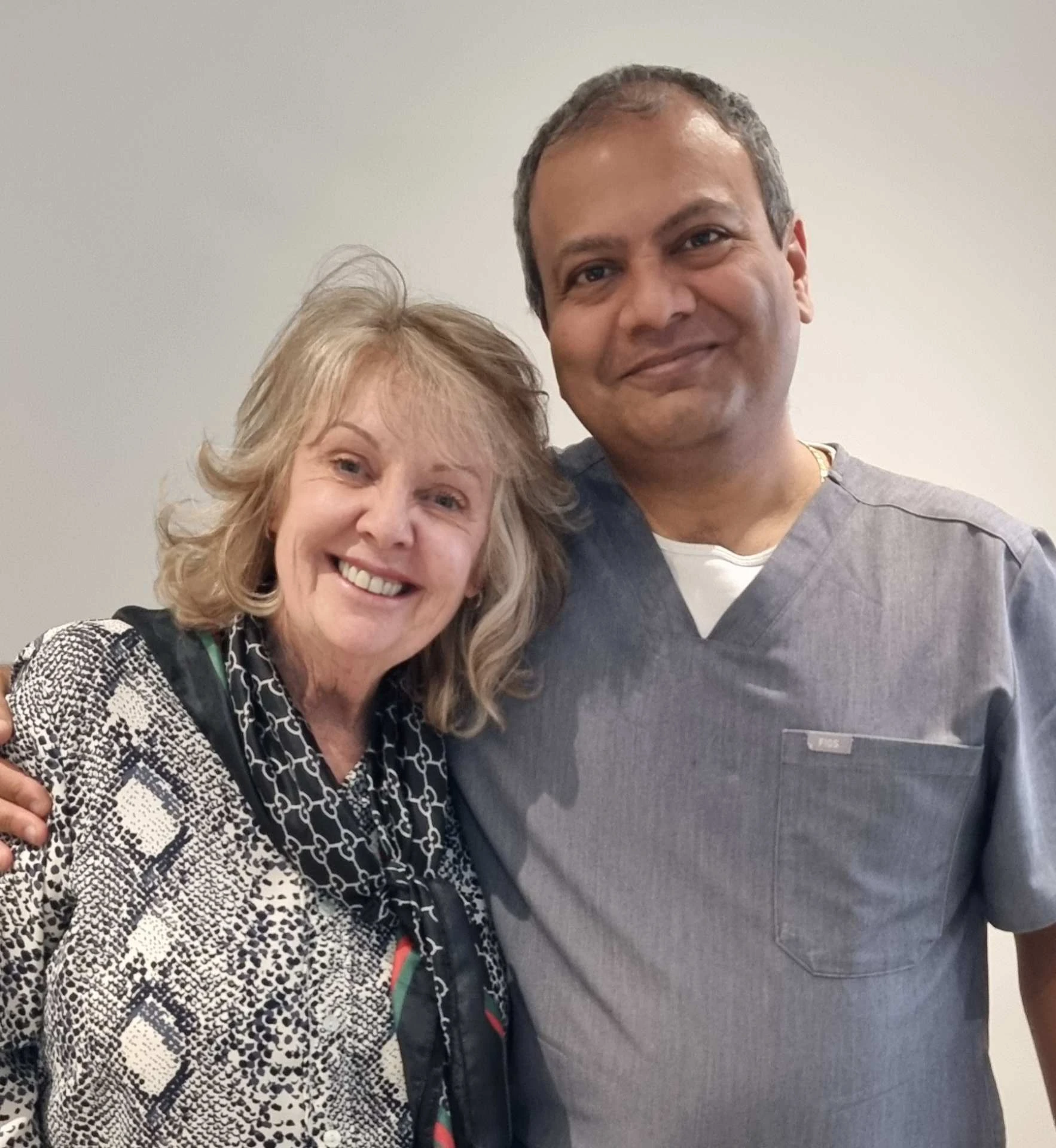 Dentist and elderly female patient smiling side by side in clinic.